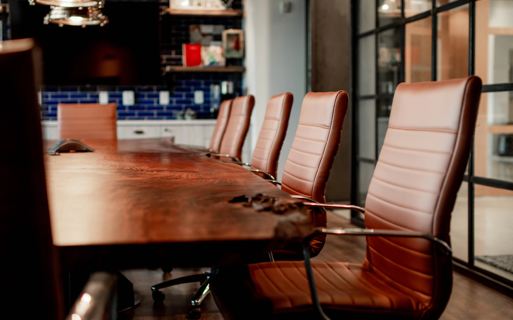 A polished wooden conference table with warm leather chairs in a glass-walled meeting room
