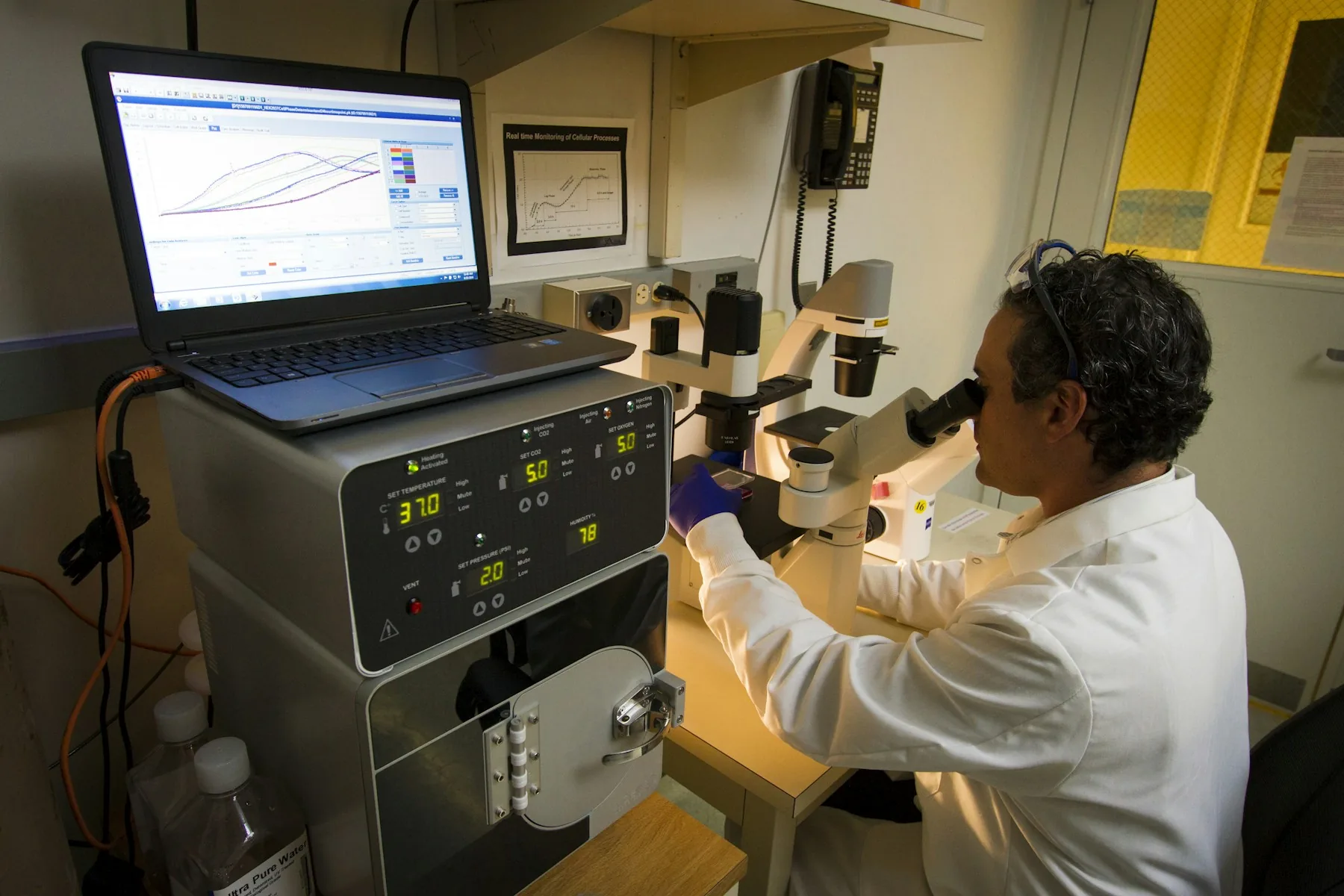 A laboratory technician examining cells under a microscope at the Cancer Genomics Research Laboratory