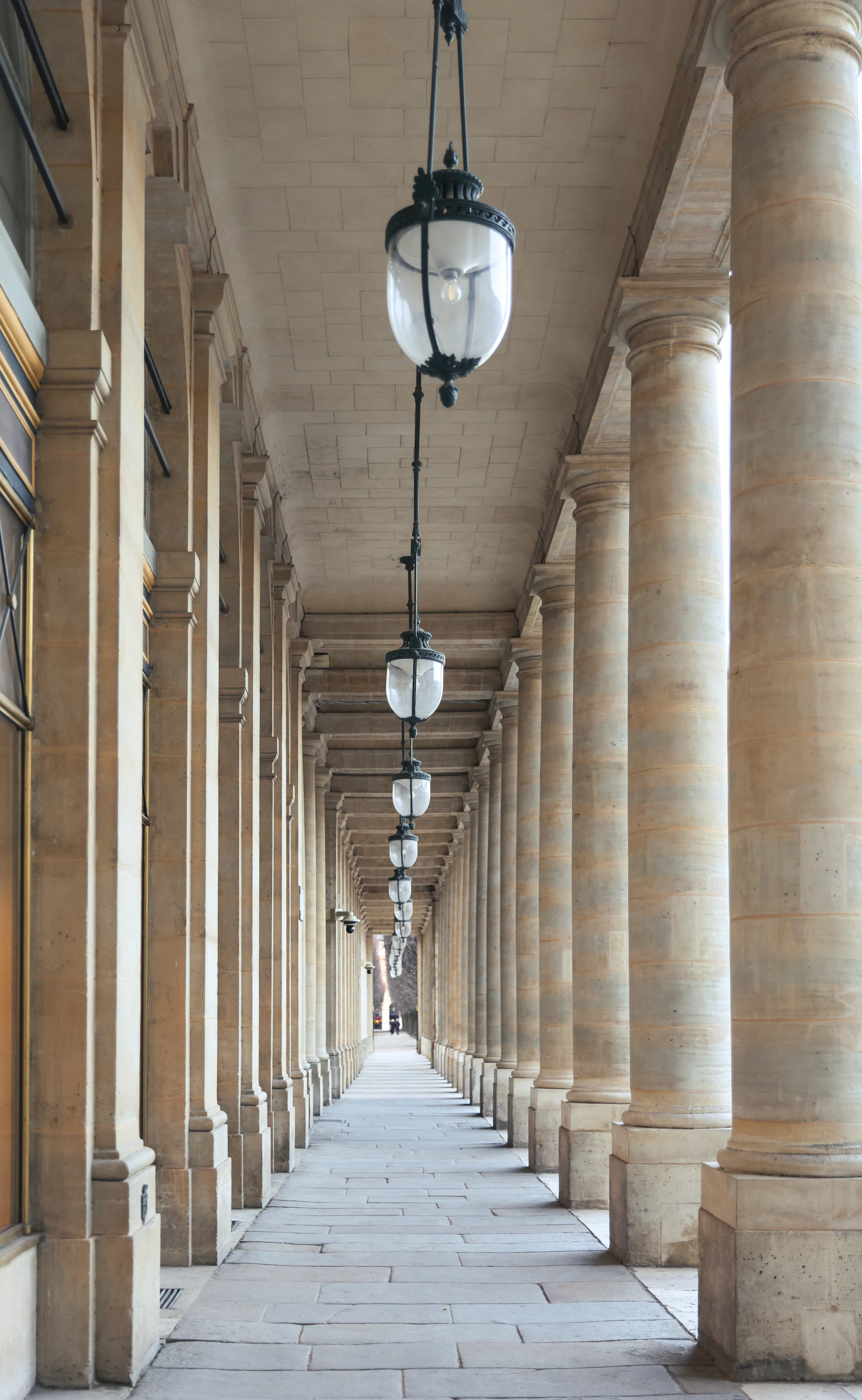 A classical stone colonnade with hanging lanterns and a long, symmetrical perspective