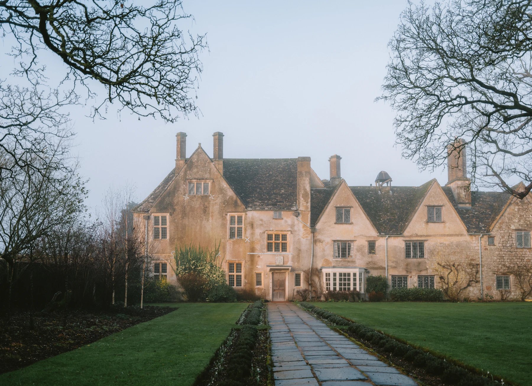 A stone manor house beyond a long garden path and clipped hedges